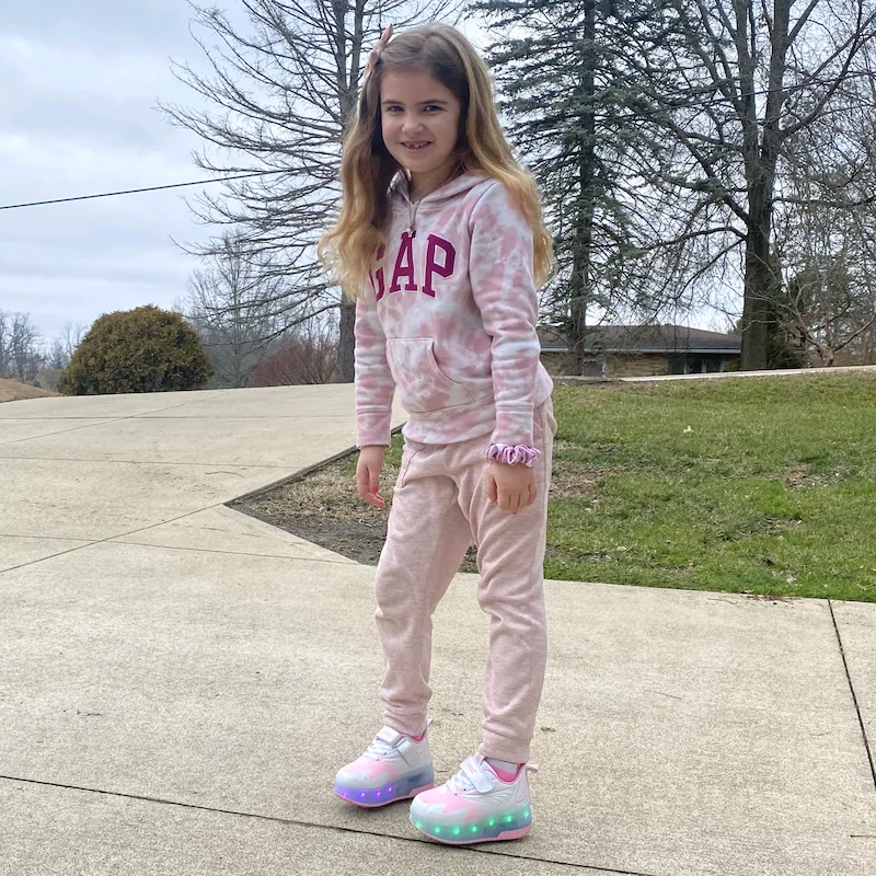 Little girl in pink outfit with pink‑white LED light‑up wheeled shoes in residential yard