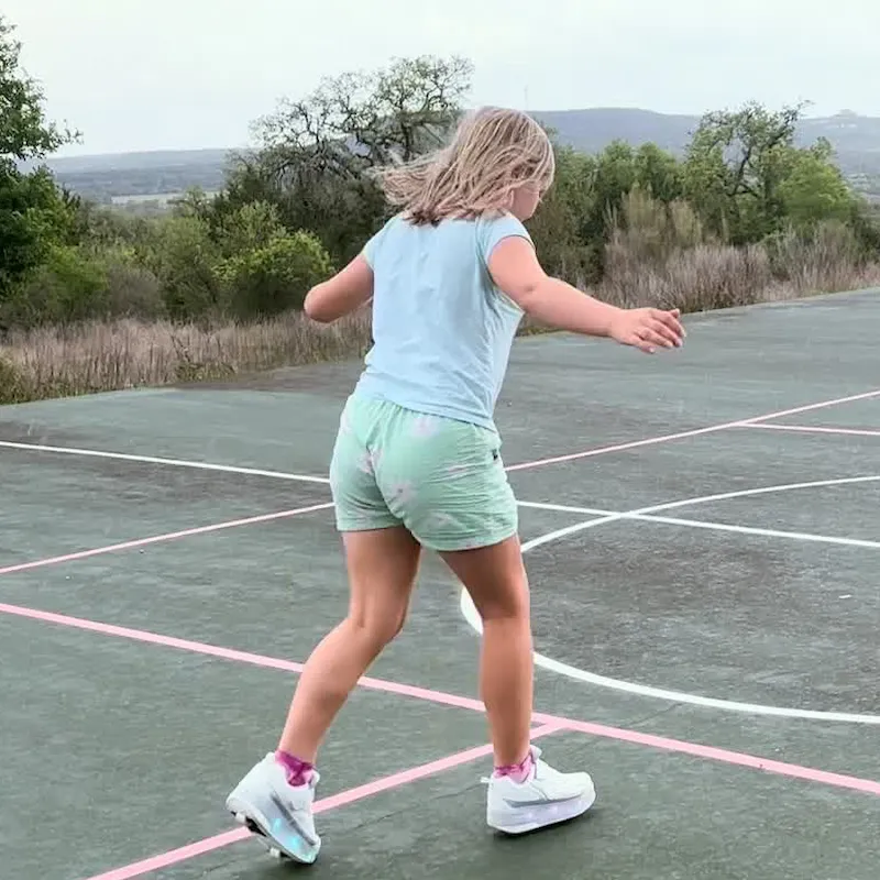 Girl skating in white LED light‑up wheeled shoes on outdoor basketball court