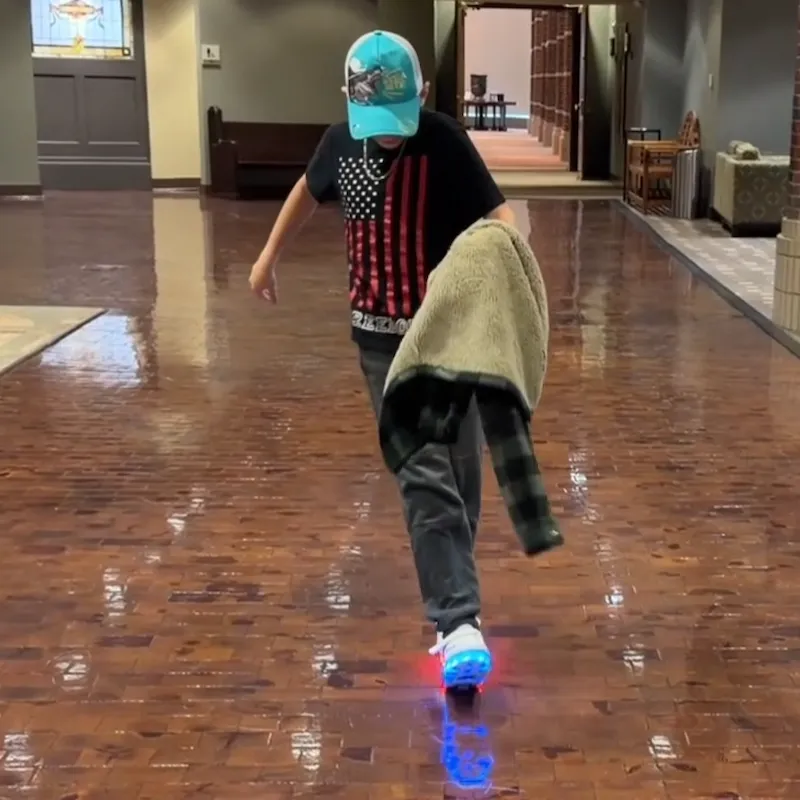 Boy sliding with LED light‑up wheeled shoes on indoor wooden floor